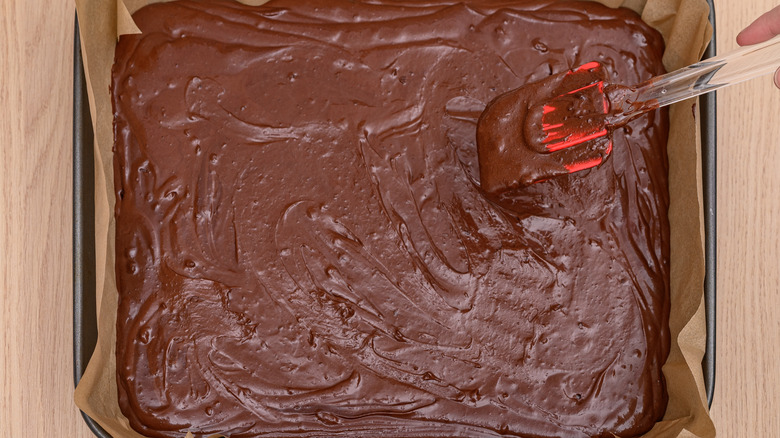 Spatula smoothing brownie batter poured into baking dish.