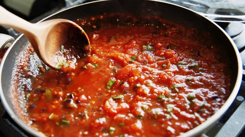 Pasta sauce being stirred in a pan with a wood spoon.