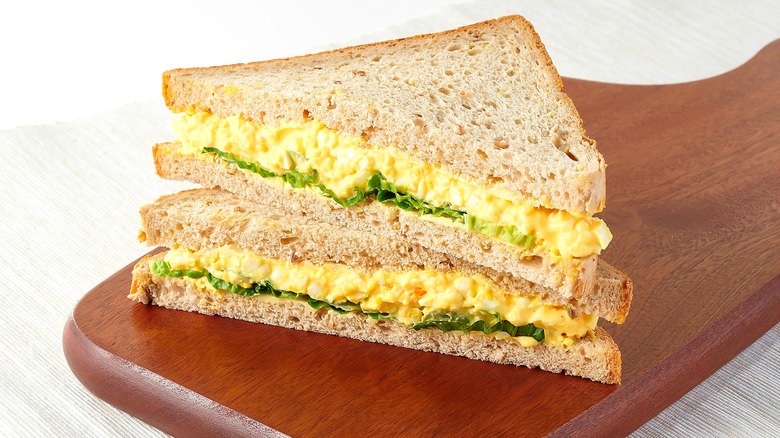 Halved and stacked egg salad sandwich with lettuce on wheat bread