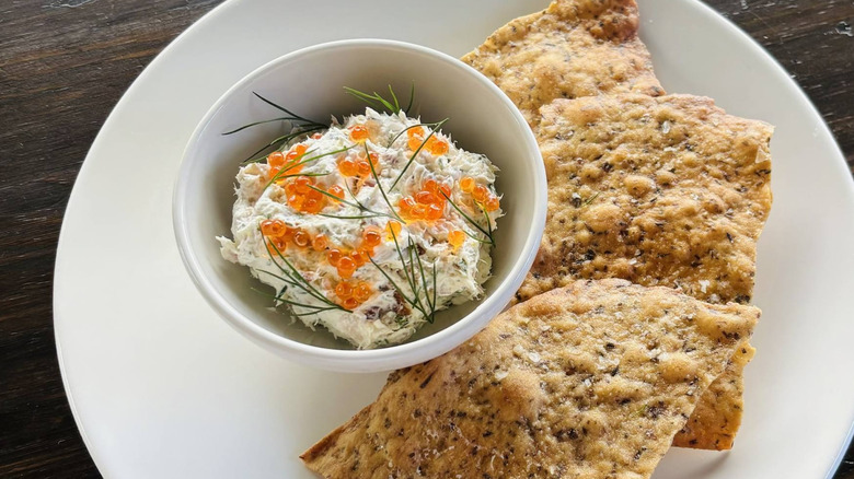A bowl of whitefish dip with roe on a plate with rice crackers from Bûcheron in Minneapolis