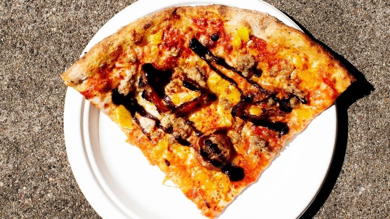 A slice of Red Wagon pizza with soppressata, banana peppers, cheese, sausage, chili flakes, garlic salt, and fig balsamic