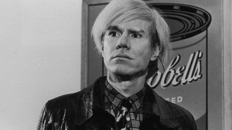Artist Andy Warhol standing in front of one of his famous Campbell's Soup paintings