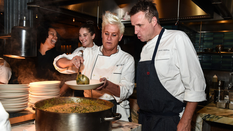 Anne Burrell serving food in a plate next to chefs in a kitchen