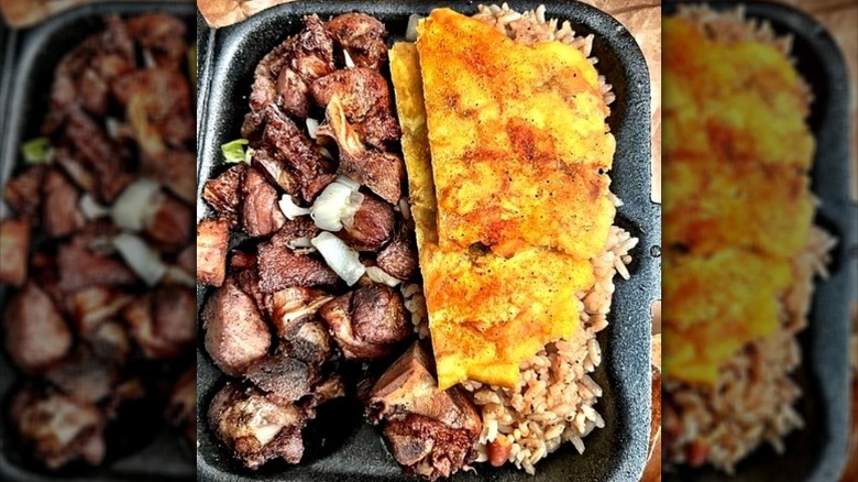 A plate of Haitian griot with rice and sides in black to-go container from Chef Creole.
