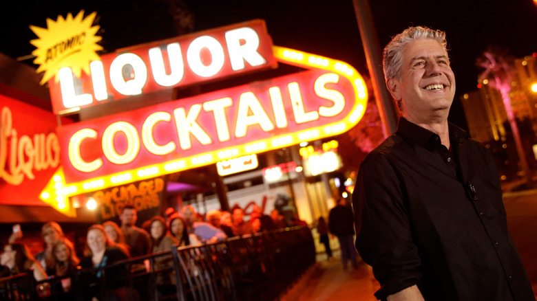 Anthony Bourdain standing in front of a neon sign that says Liquor and Cocktails