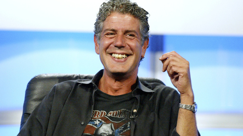 Anthony Bourdain smiling while sitting with one arm partially raised.