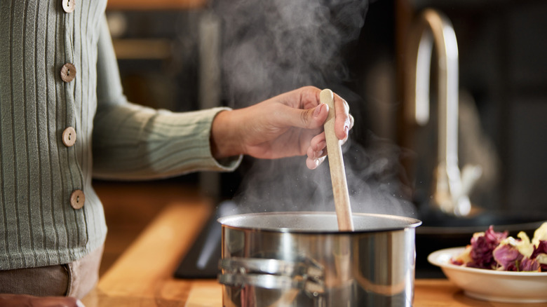 Woman using a wooden spoon to stir steaming liquid in a stainless steel pot