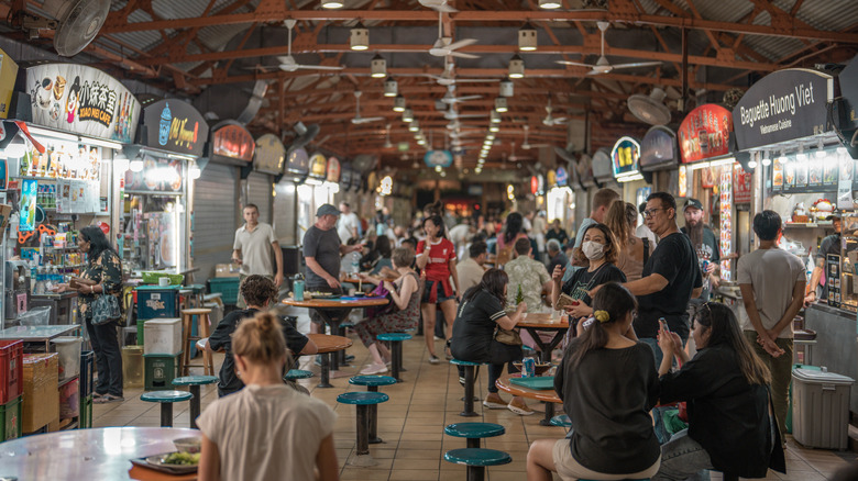 People seated and walking around Singapore's Maxwell Food Center, a popular street food hub
