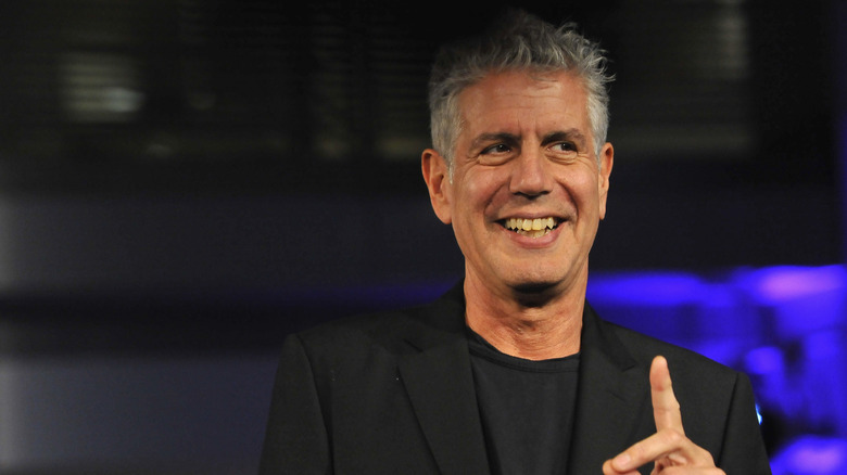 Chef Anthony Bourdain smiling and holding up an index finger