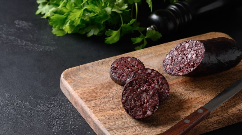 Blood sausage on wooden board with herbs and knife