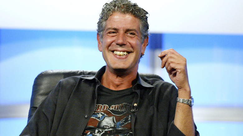 Anthony Bourdain smiling while sitting with one arm partially raised.