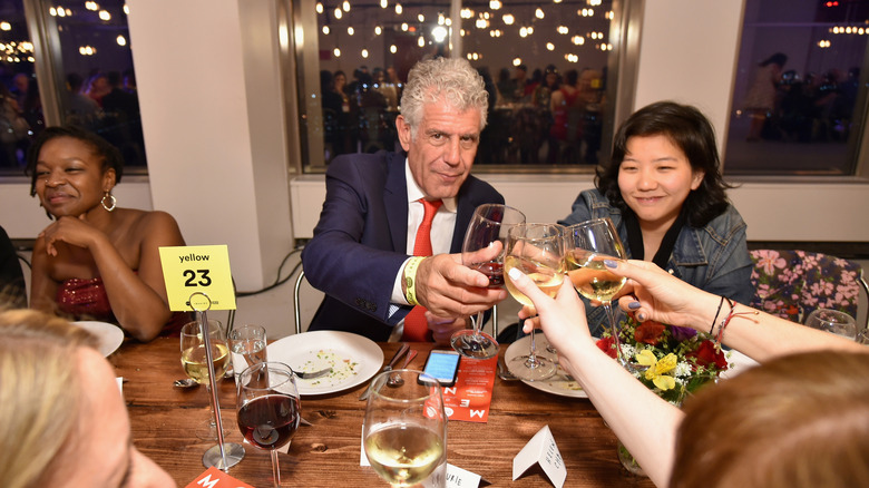 Anthony Bourdain clinking wine glasses with others at a dinner table