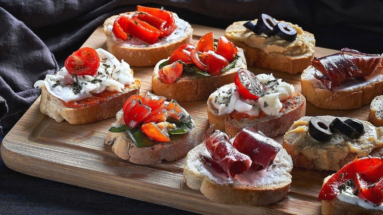 Crostini with various toppings like chopped tomatoes, sliced olives, creamy sauce, and cured meat