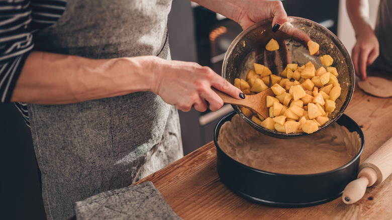 Person pouring apple filling into baking pan her daughter standing beside her and helping