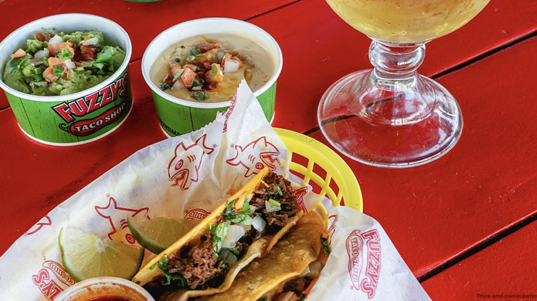 Several menu items on top of a red table alongside a beer with lime from Fuzzy's Taco Shop