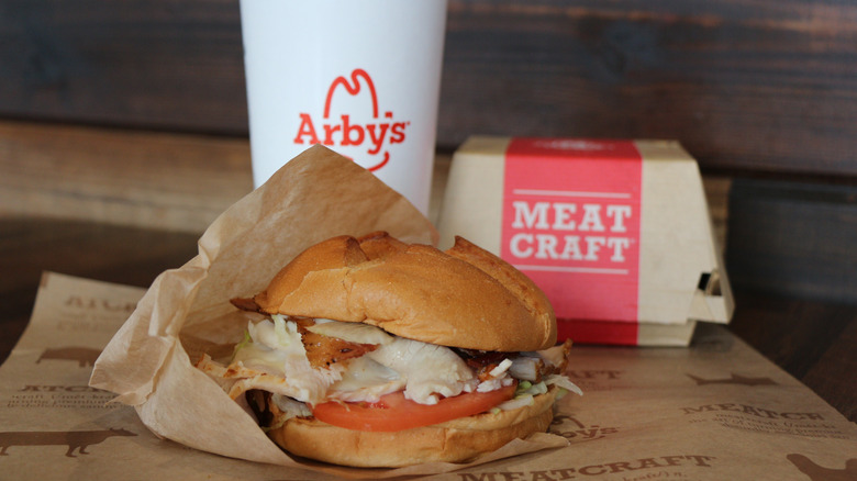 An Arby's order that features a hearty meat-stacked sandwich and a drink behind it