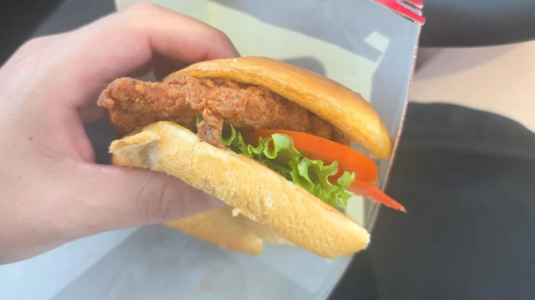 Someone holds a Chick-fil-A deluxe chicken sandwich with fried chicken, tomato, and lettuce