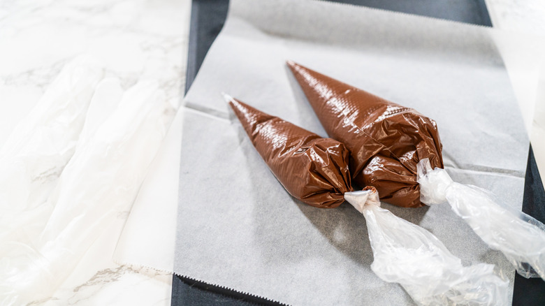 Chocolate frosting in piping bags on parchment paper