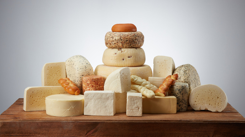 A wide variety of white cheeses stacked on a wooden table top