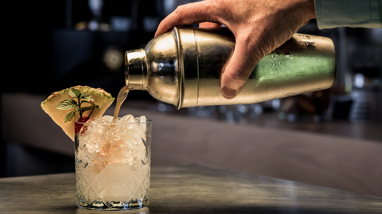 Hand pouring cocktail drink from shaker