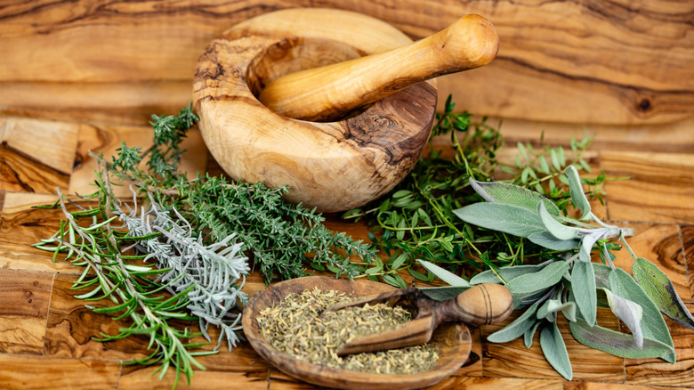 A display of fresh herbs and dried herbs on a wooden tabletop with a mortar and pestle