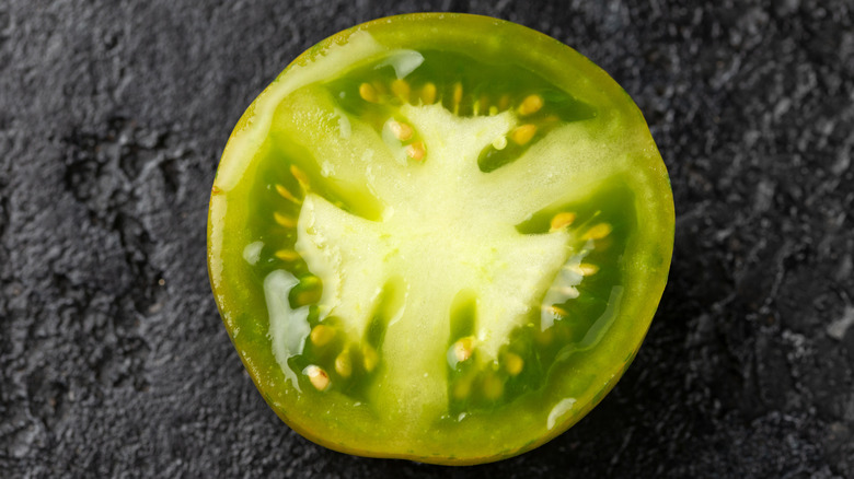 A halved fresh Green Zebra tomato on a black background