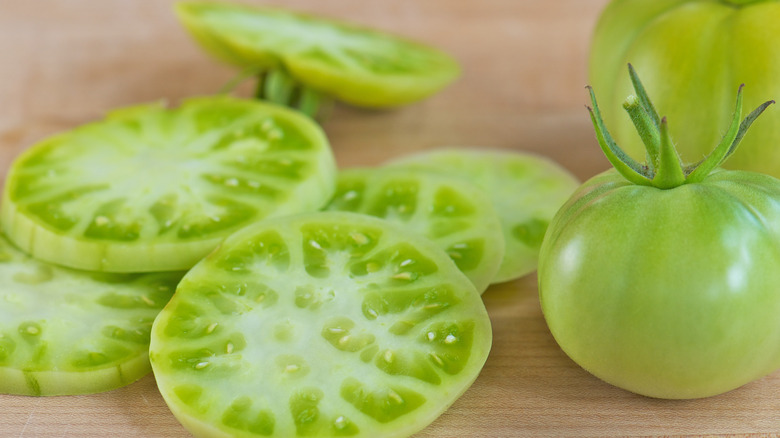 Slices of green tomato next to two whole green tomatoes