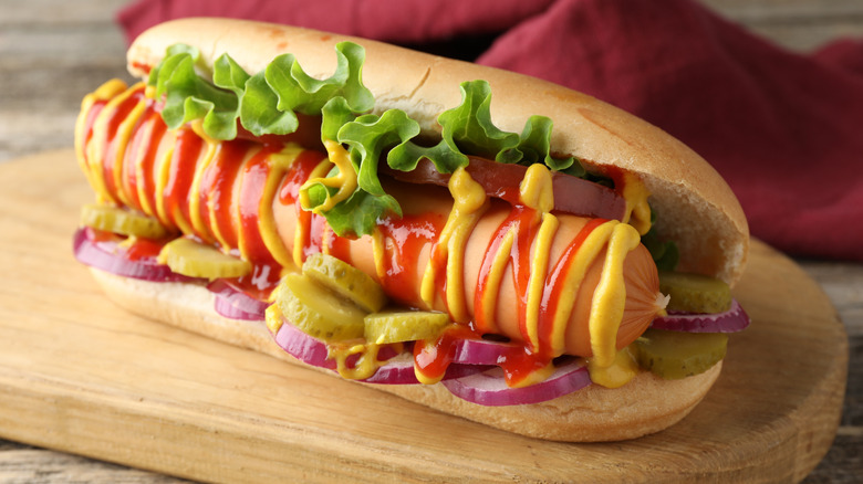 Tasty hot dog with vegetables, mustard and ketchup on wooden table, closeup