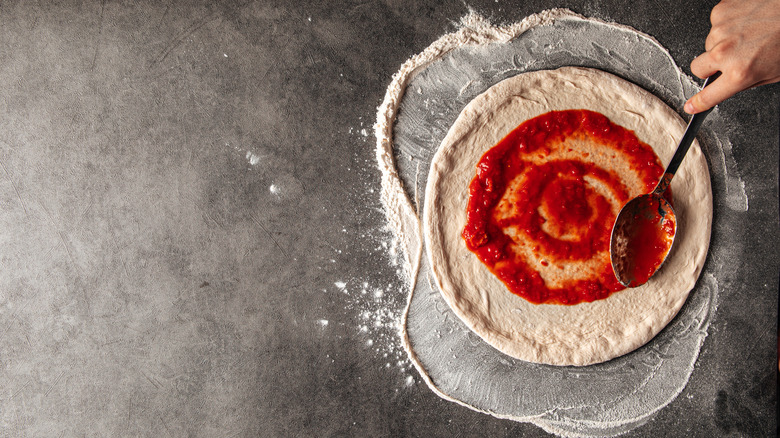 An individual spreading tomato sauce on a pizza dough.