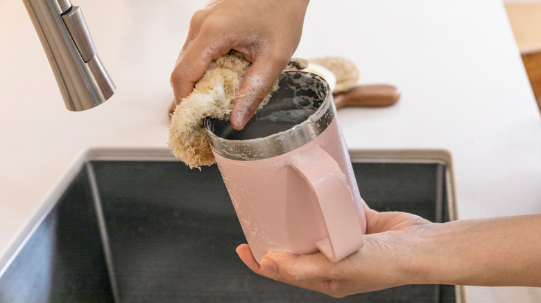 A person hand-washing a travel mug with soap
