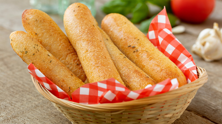 Garlic breadsticks in a basket on a wooden table