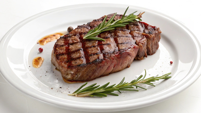 Grilled ribeye steak on a white plate with rosemary garnish