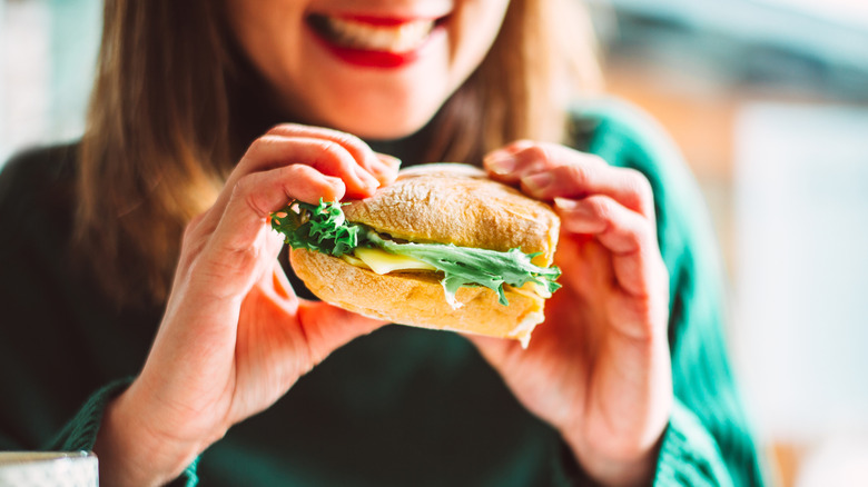 a smiling woman holding a sandwich