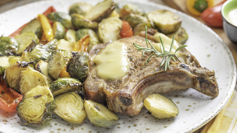 A roasted pork rib chop served with brussels sprouts and other vegetables on a plate.