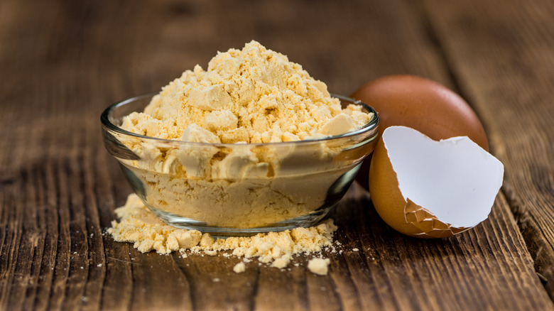 Powdered egg in a glass bowl next to a brown eggshell