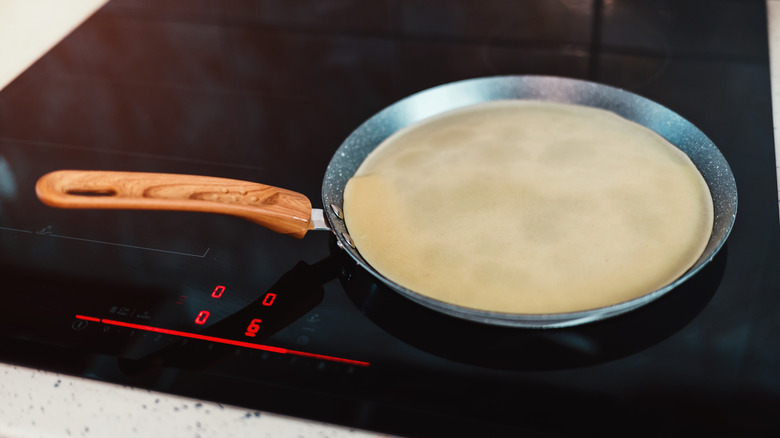 enamel crêpe pan with a wooden handle on a stove
