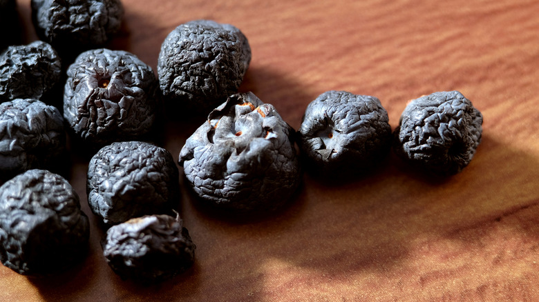 Several wrinkled blueberries on a wooden surface.
