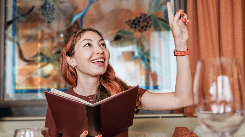 person holding a menu in a restaurant and signaling waiter