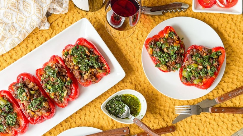 Argentinian picadillo beef-stuffed bell peppers on serving platter and plates with wine and chimichurri sauce