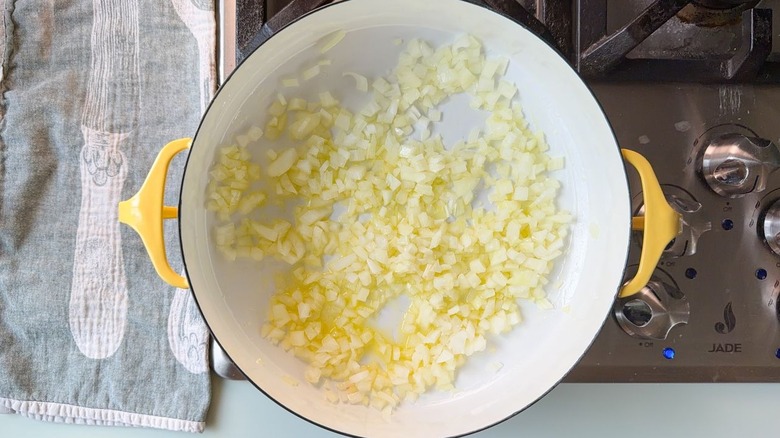 Diced yellow onion cooking in olive oil in yellow pot on stovetop