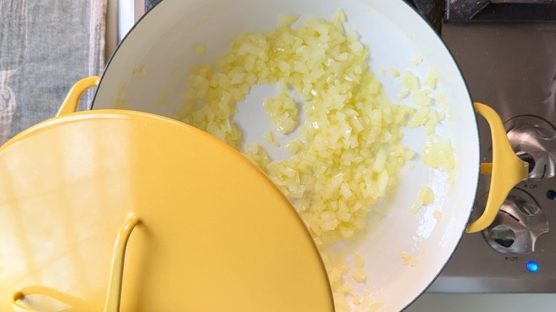 Partially covered diced yellow onion cooking in olive oil in yellow pot on stovetop