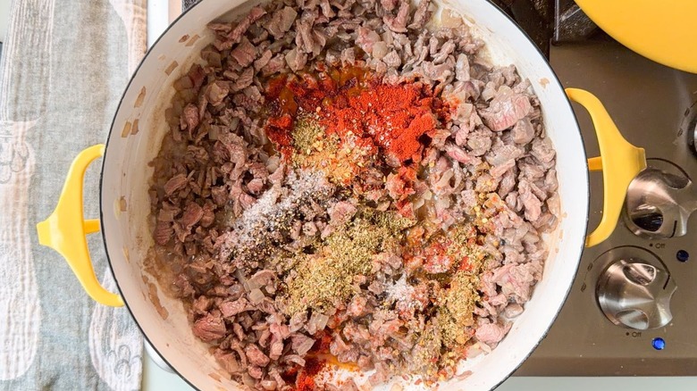 Browned cubed flatiron steak and diced onion with spices in yellow pot on stovetop