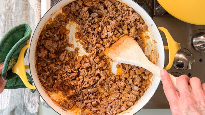 Stirring picadillo beef in yellow pot on stovetop with wooden spoon