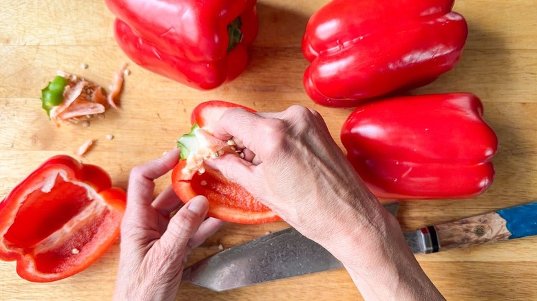 Red bell peppers and pepper halves with stems and seeds on cutting board