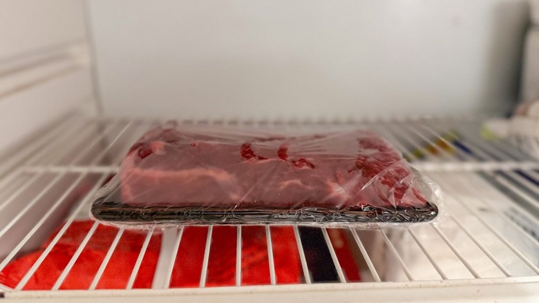 Raw flatiron steak on plastic-wrapped plate in freezer