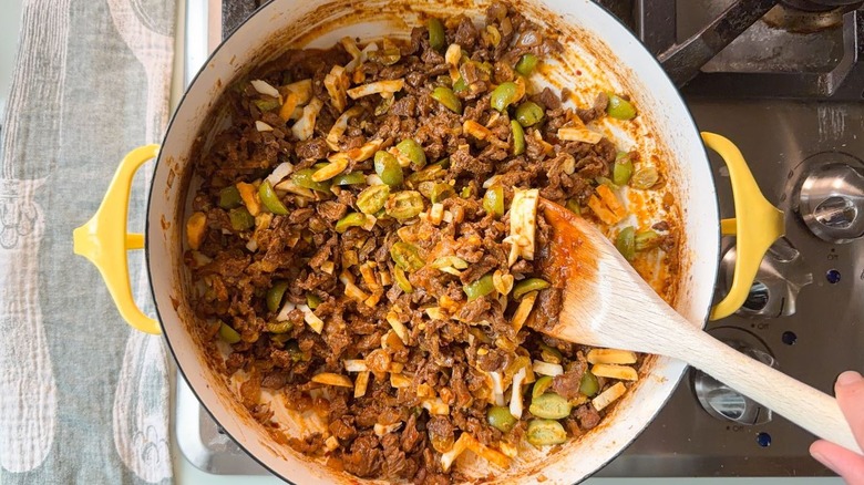 Folding chopped hard boiled egg into picadillo beef in yellow pot with wooden spoon