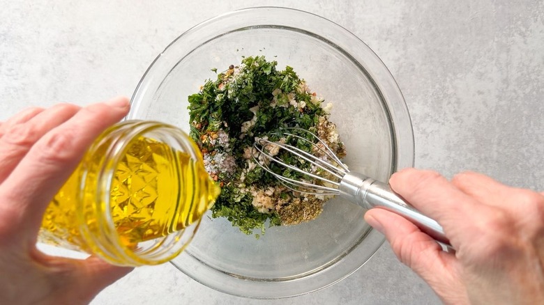Whisking olive oil into chimichurri in glass bowl
