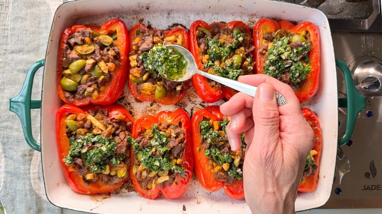 Drizzling chimichurri sauce with spoon over Argentinian picadillo beef-stuffed bell peppers