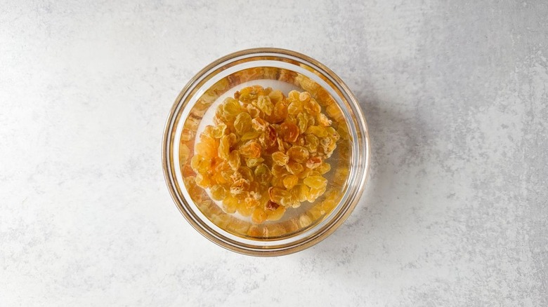 Golden raisins soaking in hot water in glass bowl