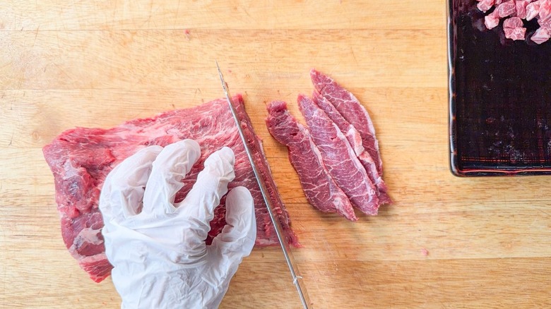 Slicing raw flatiron steak against grain on cutting board